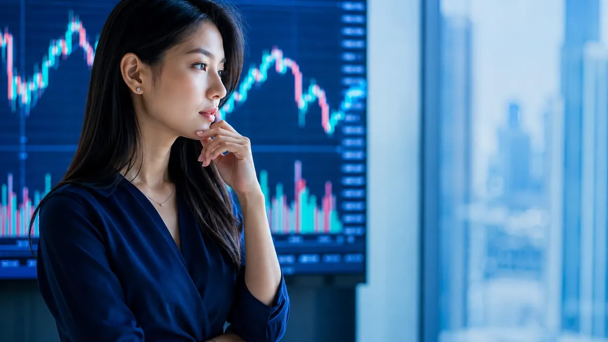 Perempuan Asia Tenggara berpikir sambil memegang dagu di depan layar grafik harga